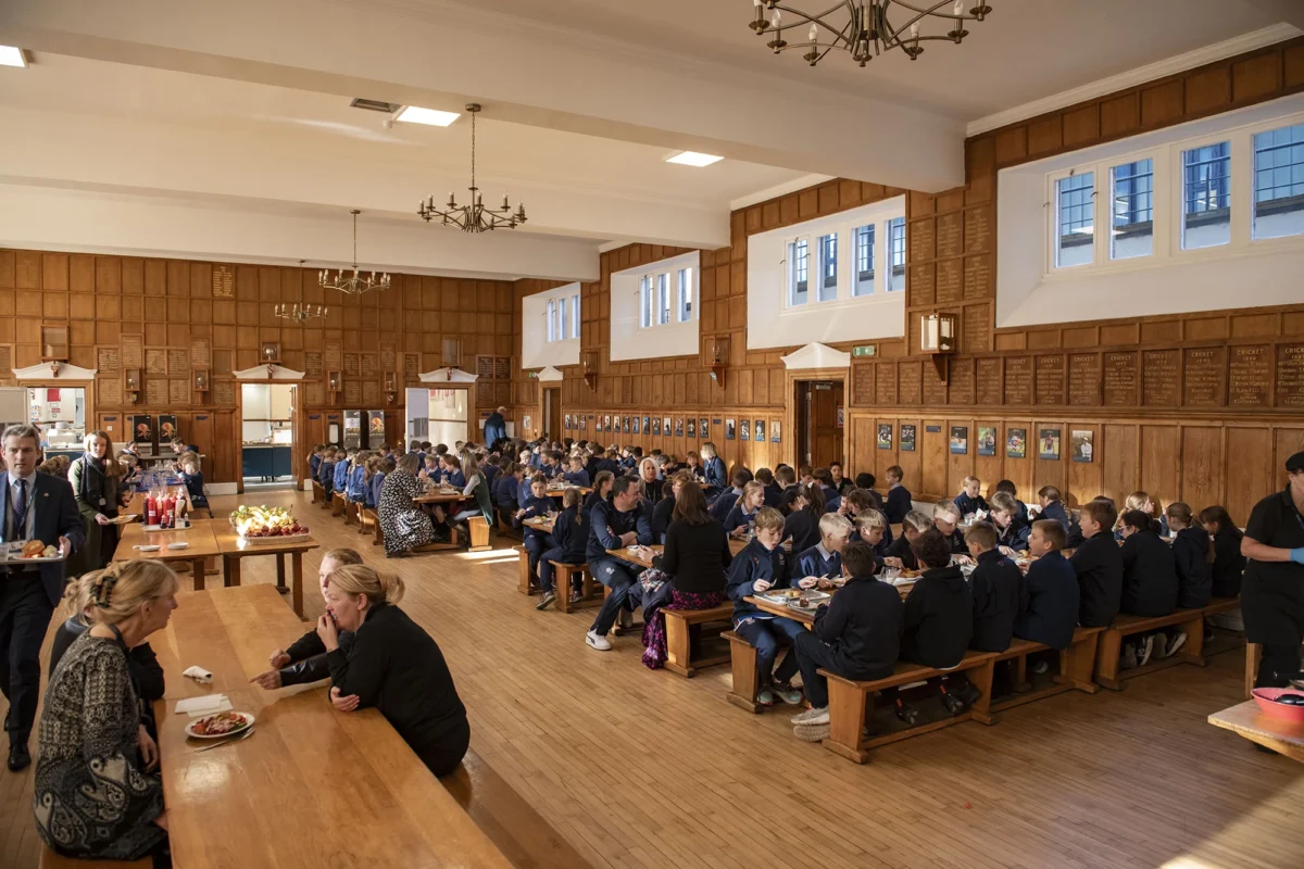 Barnard Castle School dining room filled with numerous people seated at tables, engaged in conversation and activities.