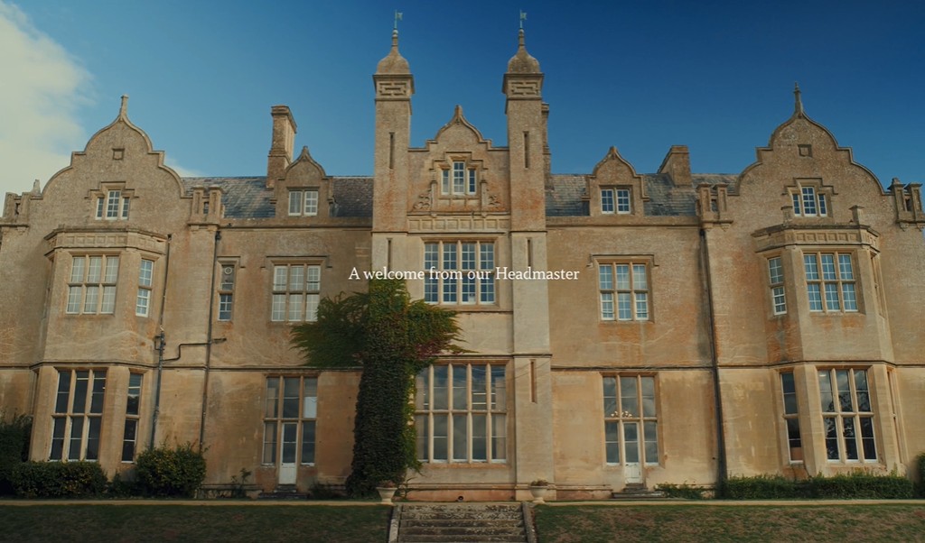 Front facade of a historic stone school building with an ivy-covered column and the text 'A welcome from our Headmaster'.