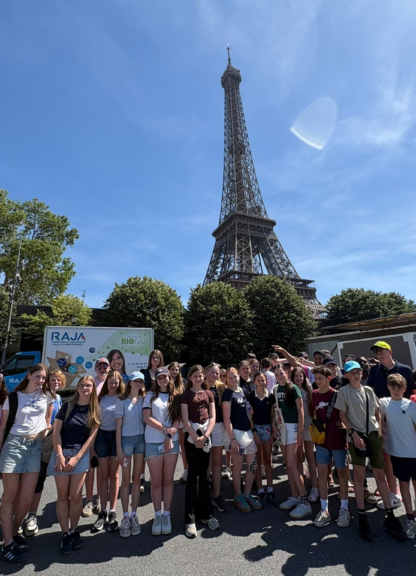 Group of students posing for a photo in front of the Eiffel Tower on a sunny day with blue sky.